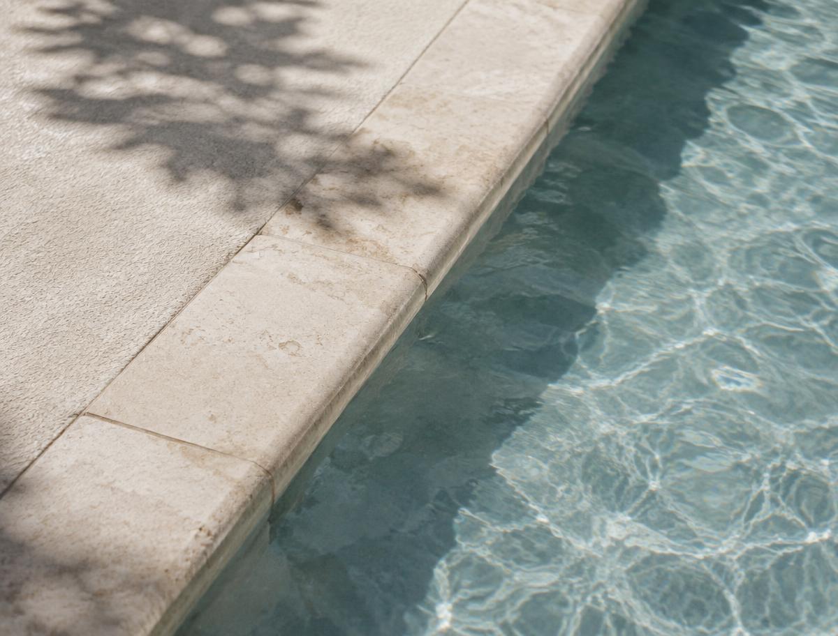 Detalhe da borda de pedra de uma piscina com sombra de folhagem